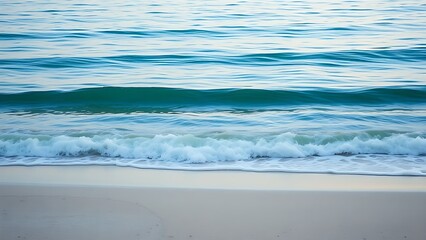 Obraz premium Tranquil sandy beach shoreline with gentle blue waves under soft morning light.