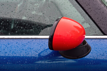 Close-up of Red Side Mirror on a Blue Car in Rain. Close-up of a bright red side mirror on a modern...