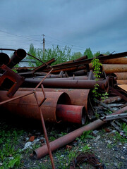 Piles of rusted metal pipes and scrap materials in an industrial area during overcast weather