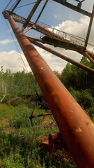 Old rusted crane stands tall among green trees under blue sky during daytime in an abandoned industrial site