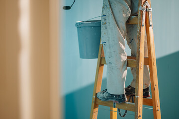 Painter working on wooden ladder painting wall with roller