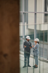 Engineers wearing suits and hard hats discussing using tablet in modern office building