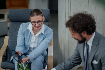 Businesswoman showing tablet to businessman while sitting in armchairs