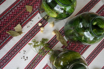 Pickled cucumbers in a jar with garlic, bay leaf, pepper and dill on the embroidered tablecloth,...