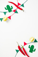 Bright Mexican flat lay featuring red chili peppers, lemon halves, green felt cacti, and colorful paper bunting on white.