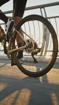 Legs of unknown young lady in cycling shoes and sportswear who is riding sports bike along bridge near a sea beach. Sunny day
