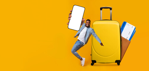 A traveler joyfully interacts with a mobile application in front of a bright yellow suitcase....