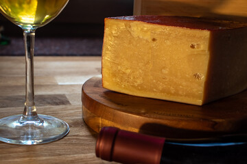 Large block of golden cheese with reddish rind on wooden board labeled parmesan accompanied by a...