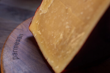 Large textured golden wedge of parmesan cheese with dark rind on wooden board distinctly labeled parmesan