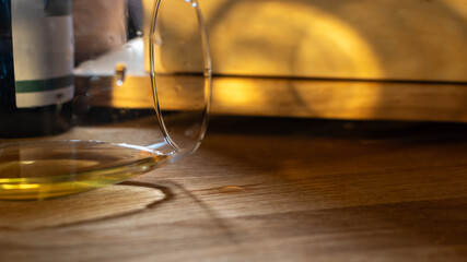 Partially filled clear glass with amber liquid on wooden surface, where small spill is visible next...
