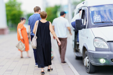 People boarding a minibus on a busy street in an urban area during a sunny day