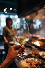 A hand holds a glass of wine in a vibrant kitchen preparing a delicious meal as a friend chats in the background creating a warm atmosphere