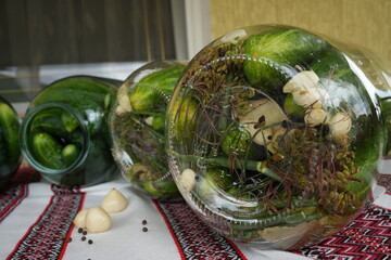 Pickled cucumbers in a jar with garlic, bay leaf, pepper and dill on the embroidered tablecloth,...