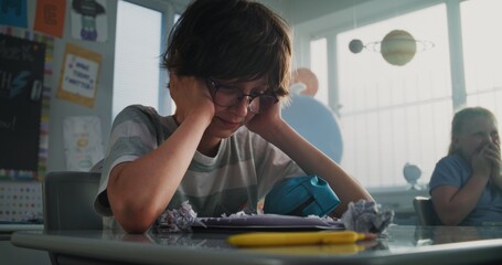 Stressed Primary School Boy Sitting Alone at Desk in Classroom While Aggressive Classmates Abusing Him, Throwing Papers and Laughing. School Bullying, Peer Harassment and Toxic School Environment.