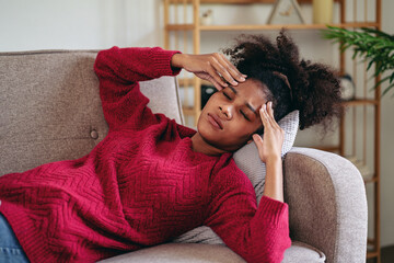 Woman Experiencing Headache, Migraine, Stress Relief on Couch. Black Adult Feeling Pain, Sick, Unwell. Health Problem and Fatigue Concept for Medical Content