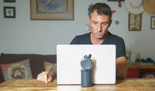 Man works on laptop in living room. The man is forty years old, of Caucasian origin and wears a black t-shirt - Powered by Adobe