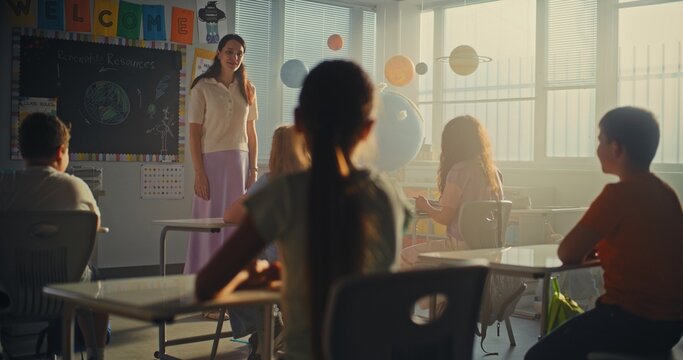 Female Teacher Finishing the Lesson, Announcing the End of School Day to Diverse Kids. Elementary School Students Standing Up, Packing Their Backpacks and Leaving Modern Classroom. Slow Motion.