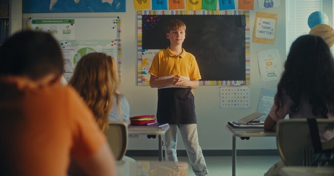 STEM Class on Renewable Energy: Female Teacher Calling Elementary School Student to the Board. Talented Boy Presenting Homework on Ecology in Front of Classroom Full of Diverse Children, Classmates. - Powered by Adobe