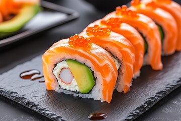 Fresh salmon sushi roll with avocado and orange roe on slate board.