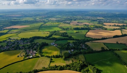Obraz premium Expansive aerial view of vibrant rural landscape with green fields, brown farmland. Small community nestled among green plants under clear sunny sky. Nature beauty, agricultural land, peaceful