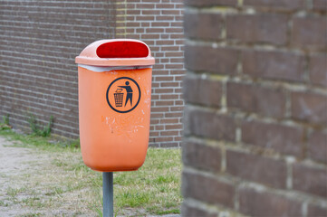 Orange Trash Can with Red Lid by Brick Wall