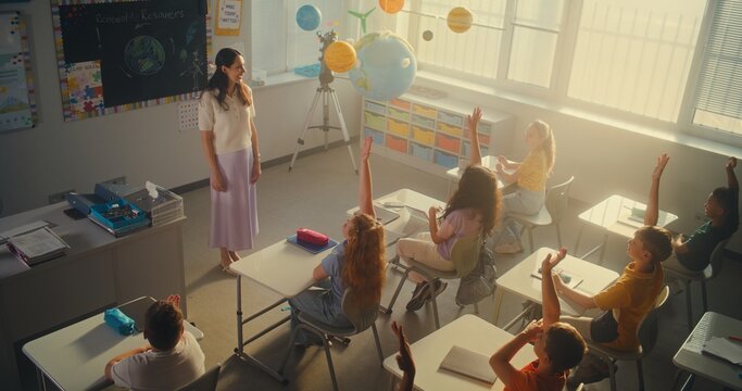 STEM Class: Female Teacher Educating Ecology to Elementary School Students in Classroom. Diverse Kids Raising Hands to Give Answer, Smart Girl Going to the Board and Presenting Homework. High Angle. - Powered by Adobe