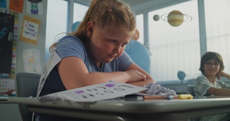 Upset Elementary School Student Sitting Alone at Desk and Crying While Classmates Bullying Her,...
