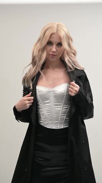 Beautiful blonde in a black cloak and a white corset and a black skirt on a gray background.
