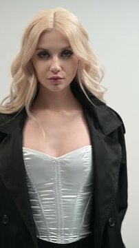 Beautiful blonde in a black cloak and a white corset and a black skirt on a gray background.
