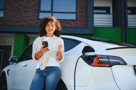 Woman using smartphone while charging electric car at home