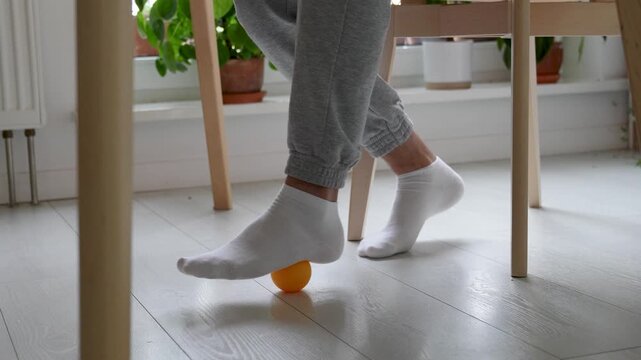 Socked feet rolling orthopedic ball to improve balance and foot mobility on floor. Flat feet correction, balance training, foot muscle activation, arch support, rehabilitation of motor skills