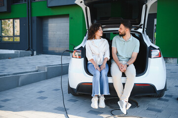 Young couple relaxing while charging electric car at home