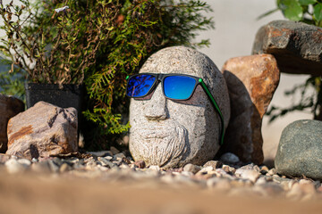 Creative shot in the garden of a stone head near a bush of flowers on gravel. High quality photo