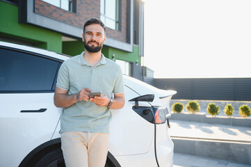 Man using smartphone while charging electric car at home