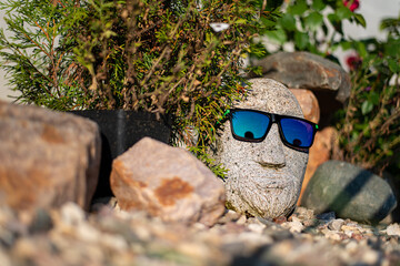 Creative shot in the garden of a stone head near a bush of flowers on gravel. High quality photo