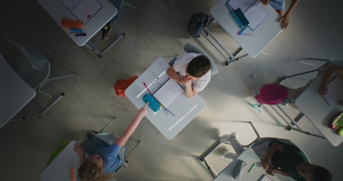 Depressed Primary School Boy Sitting Alone at Desk in Classroom While Aggressive Classmates Abusing Him, Throwing Papers and Laughing. School Bullying and Toxic School Environment. Rotating Top View. - Powered by Adobe