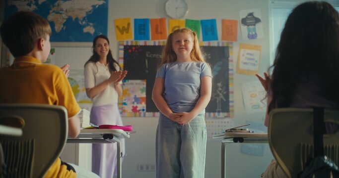 Shy Primary School Girl Showcasing Knowledge of Ecology in Front of Class and Teacher. Smart Kids Sitting at Desks During Environmental Science Lesson in Modern Classroom. STEM Education. Slow Motion.