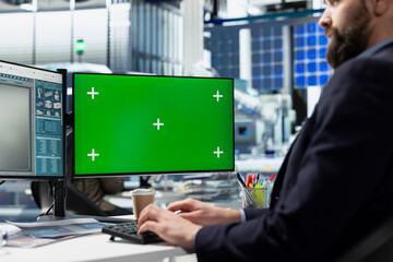 Solar operations employee conducts system check next to green screen in a busy factory, ensuring...