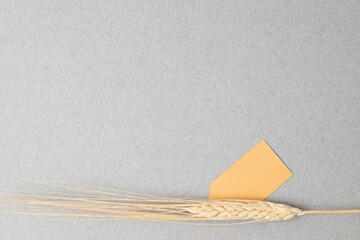 Minimalistic background with wheat grass, golden yellow gift tag on a gray surface, copy space.