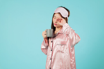 Asian woman in pajama holds a cup after a light sleep, wearing a sleep mask, and relaxing at home,...