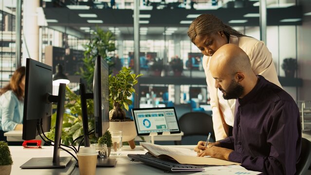 Accountant in busy modern startup agency working on PC, interrupted my manager asking him to check reports. Businessman working in office, tasked by supervisor to crosscheck paperwork data, camera B - Powered by Adobe