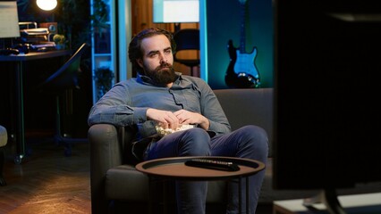 Sad man on couch eating popcorn from stress while watching heartbreaking drama movie on streaming service. Person consuming snack, distressed by TV show favorite character dies, camera A