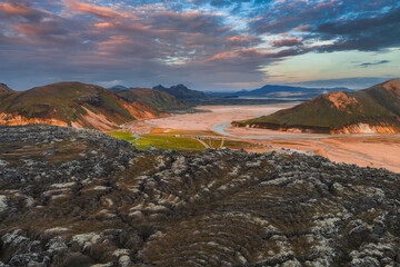 Aerial view of Landmannalaugar in Iceland with vibrant rhyolite mountains, dark lava fields, green...
