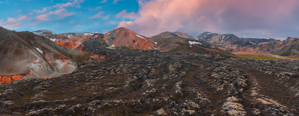 Vibrant orange, red, and brown rhyolite mountains with snow patches, rugged lava fields, and a...