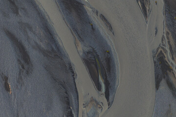 Braided river channels flow through dark volcanic sands in Iceland, with silvery water contrasting...
