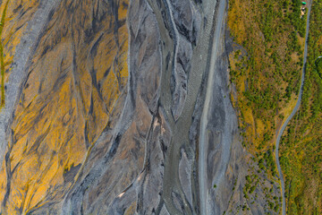 Aerial image of a braided river in Iceland with gray and yellow sediment, lush green vegetation, and a winding road on the right.