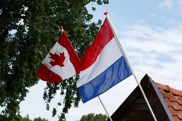 Flags of Canada and the Netherlands wave together on a sunny day at a cultural event celebrating friendship and unity