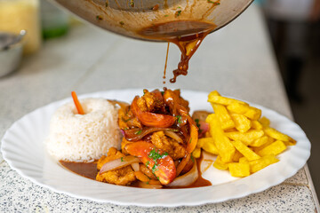 Chef pouring sauce on traditional peruvian fish dish with rice and french fries