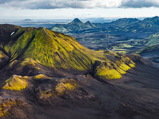 Aerial view of a green moss covered mountain surrounded by dark volcanic terrain in Iceland, with...