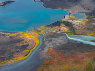 A turquoise lake surrounded by dark volcanic terrain, with vibrant yellow, orange, and red...